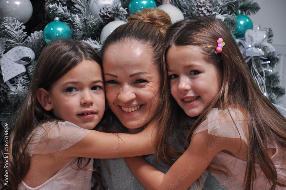 Two little girls hugging their mom. Smiling daughters hugging mom for Christmas Two little girls hugging their mom. Smiling daughters hugging mom for Christmas