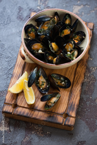 Boiled mussels in a bowl on a wooden serving board, studio shot, selective focus