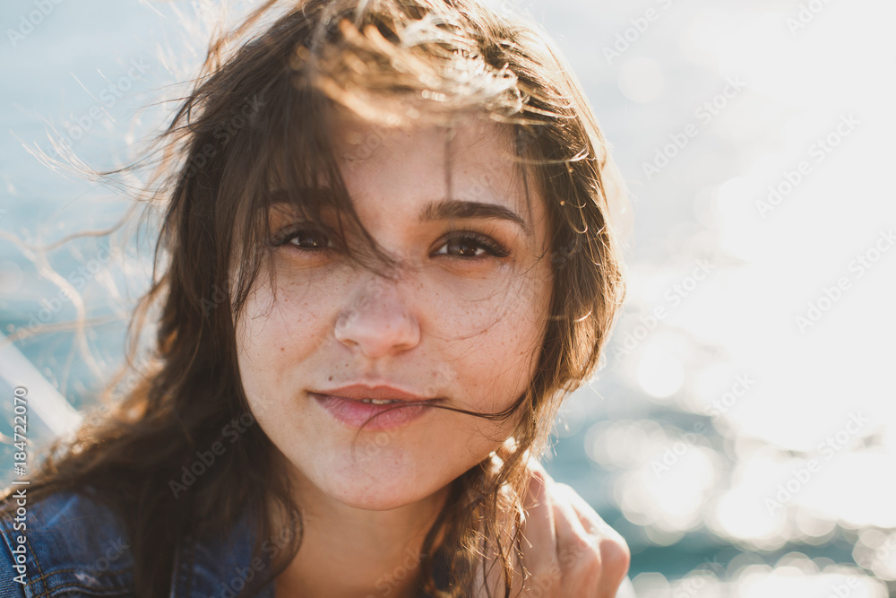 Beautiful young woman at the ocean standing against a turquoise blue sea with her hair blowing in the breeze Beautiful young woman at the ocean standing against a turquoise blue sea with her hair blowing in the breeze