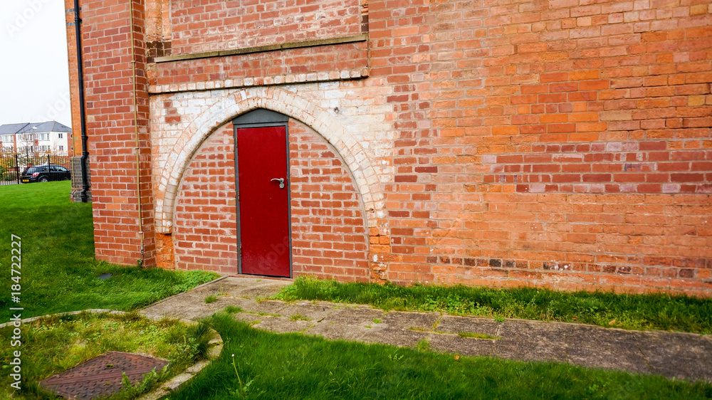 Brick wall with red door under arch