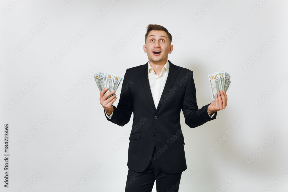Young successful handsome rich business man in black suit holding wad of cash dollars isolated on white background for advertising. Concept of money, achievement, career and wealth in 25-30 years.