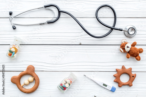Pediatrician. Stethoscope, thermometer, pills, toys near keyboard on white wooden background top view copyspace