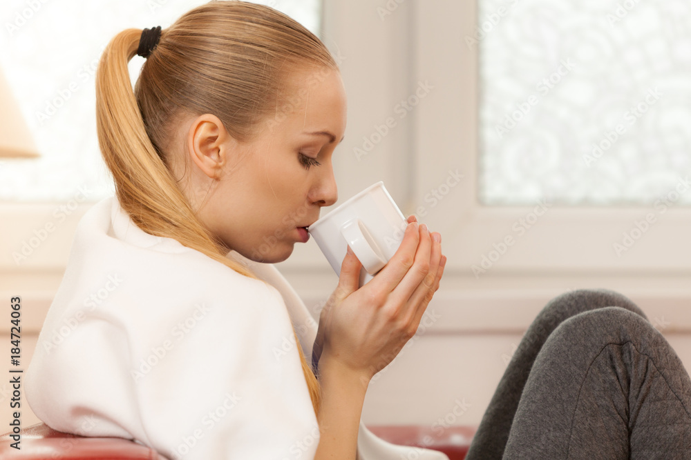 Woman lying on sofa under blanket drinking tea Woman lying on sofa under blanket drinking tea
