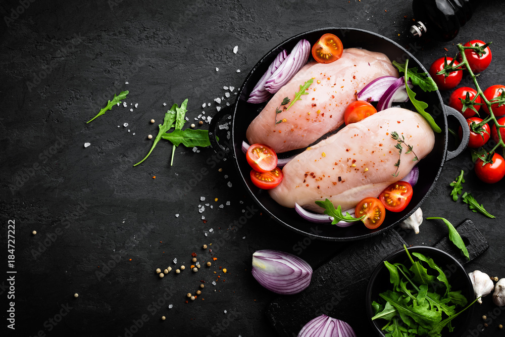 Fresh raw chicken meat, fillet marinated with spices, onion and tomatoes on black background. Top view Fresh raw chicken meat, fillet marinated with spices, onion and tomatoes on black background. Top view