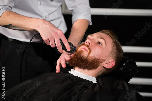 Hairdresser is shaving male beard with the knife. Handsome bearded man is getting shaved by hairdresser at the barbershop