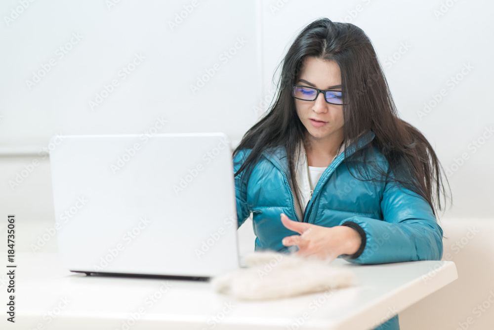 the girl wearing spectacles in casual clothes of mint color works with a laptop on the Internet the girl wearing spectacles in casual clothes of mint color works with a laptop on the Internet