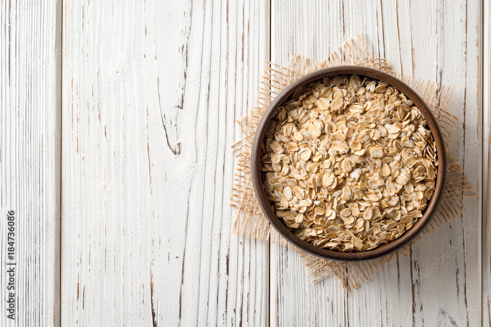 Oat flakes in ceramic bowl on white wooden table Oat flakes in ceramic bowl on white wooden table