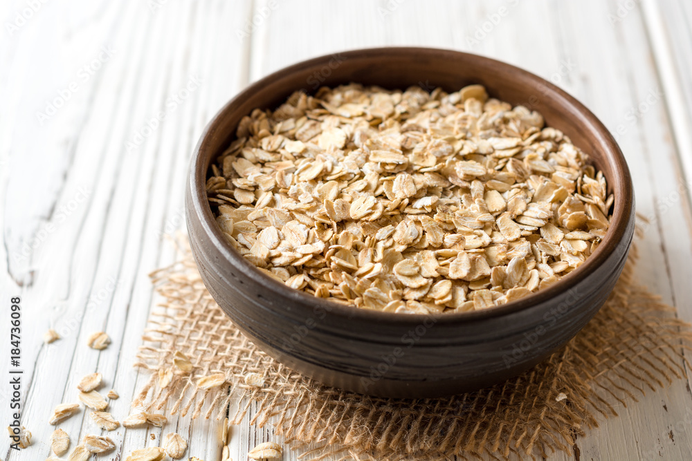 Oat flakes in ceramic bowl on white wooden table Oat flakes in ceramic bowl on white wooden table