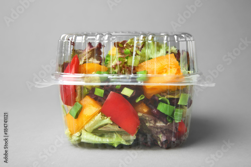 Schilderij op canvas Plastic container with salad on grey background