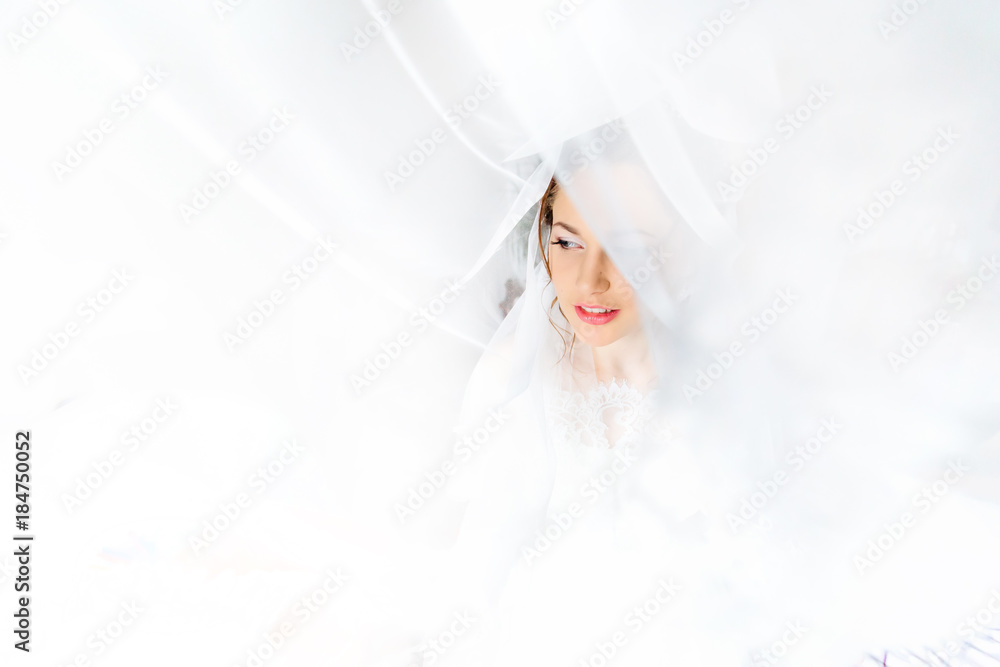 The bride in a white dress looks through the window wrapped in t
