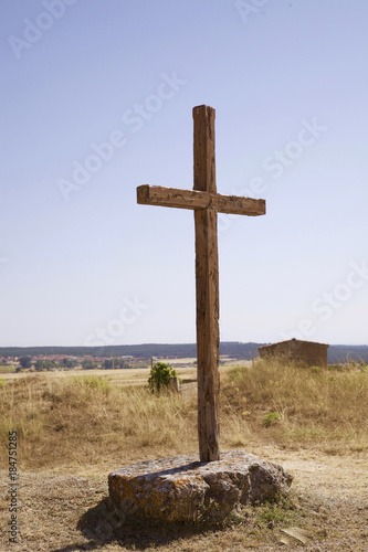 cruz símbolo religioso cristiano de madera en medio de un camino sujeta por dos grandes piedras en un campo cerca de la carretera bajo el cielo azul