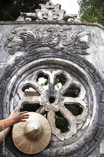monumento antiguo vietnamita con grabados esculpidos en la piedra y con una mano apoyada en el llevando un gorro típico vietnamita en forma de cono photo