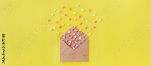 Multicolor sweets sugar candy hearts fly out of craft paper envelope on the bright yellow background . Valentine day. love concept. Gift, message for lover. Space for text. Wide banner. © okrasiuk