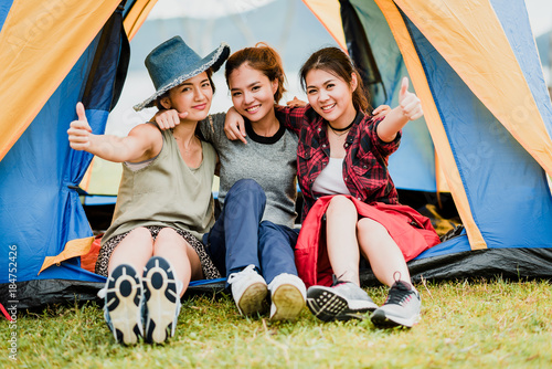 Happy three Asian girl friends smiling and show thumb up outside tent on vacation holiday. teavel with friends concept photo