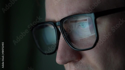 an office worker sits at the computer, a monitor with tables and graphs is reflected in the glasses.