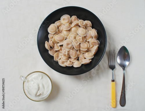 Traditional dish of dumplings in a bowl on a white tablecloth. Served with sour cream, a fork and a spoon.