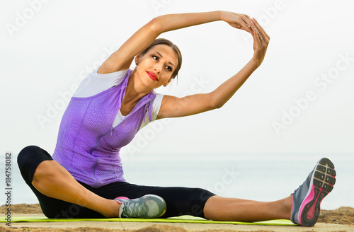 Woman practising yoga poses sitting on beach by sea
