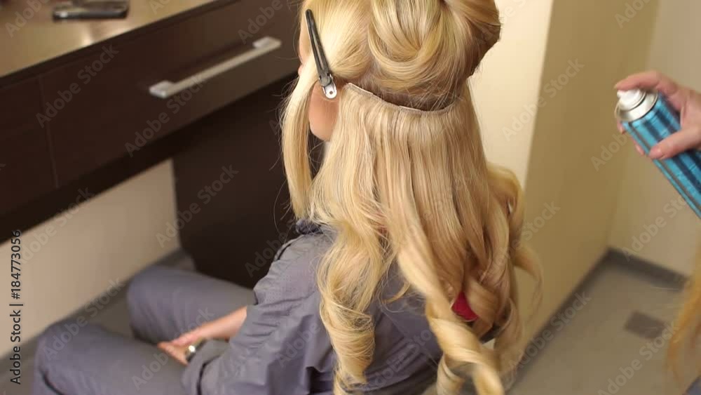 Closeup of hairdresser's hands using hairspray on client's hair at