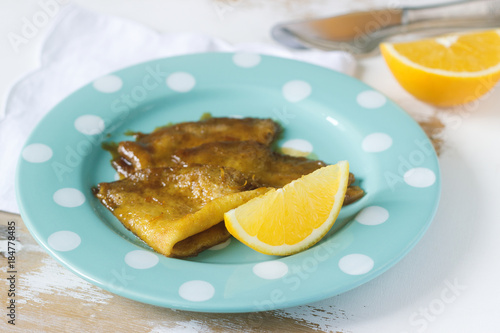 Crepe suzette in caramel sauce on a plate with a slice of orange. French dessert.