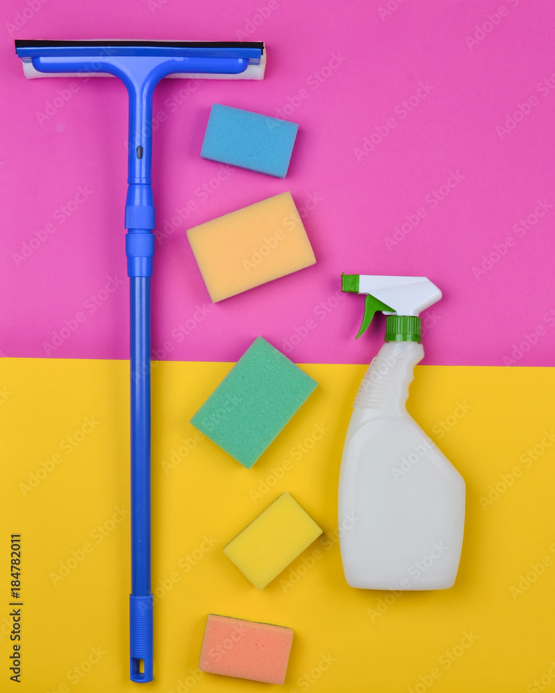 Sponges, window mop, sprinkler cleanser on a pink yellow background. Objects for home cleanliness. Products for cleaning glass windows. Top view. Trend of migimilism. Sponges, window mop, sprinkler cleanser on a pink yellow background. Objects for home cleanliness. Products for cleaning glass windows. Top view. Trend of migimilism.