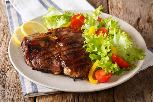 Delicious grilled T-bone steak with fresh vegetable and lemon close-up. horizontal photo