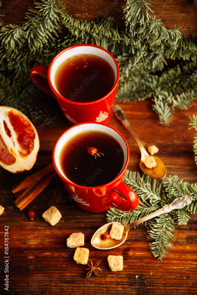 Close-up two glass cups full of hot, red, aromatic lemon tea with dark chocolate on a pine branch and table background. Winter snacks composition. Close-up two glass cups full of hot, red, aromatic lemon tea with dark chocolate on a pine branch and table background. Winter snacks composition.