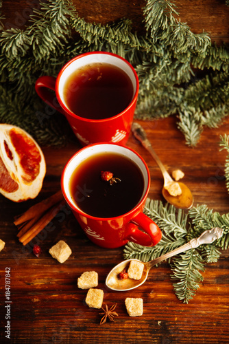Close-up two glass cups full of hot, red, aromatic lemon tea with dark chocolate on a pine branch and table background. Winter snacks composition.