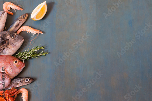 Fresh fish and seafood lay on blue wooden background with copy space.