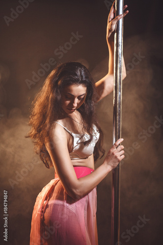 Pole dance. Slim woman in pink skirt posing with pylon.