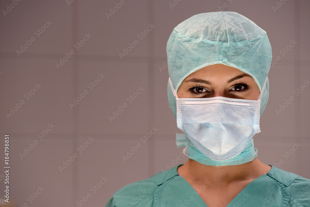 A young woman poses in an operation theater fully dressed as a theater nurse with a face mask and green sterile medical work clothing. A young woman poses in an operation theater fully dressed as a theater nurse with a face mask and green sterile medical work clothing.