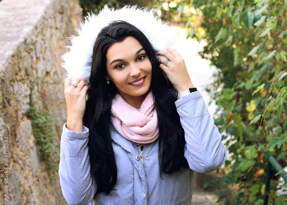 Beautiful young woman wearing winter coat with the faux - fur hood 