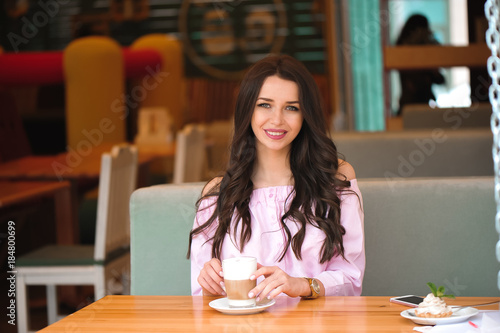 Woman drinking hot cappuccino coffee and eating cake at cafe.