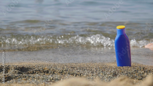 A jar of sunscreen on the beach near the sea