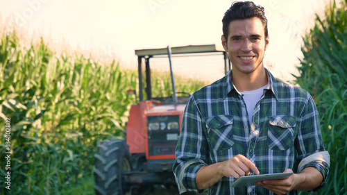 Portrait of a beautiful young farmer (student) working in the field with a tractor working in a tablet, happy, in a shirt, corn field. Concept ecology, transport, farmers, clean air, food, bio product photo