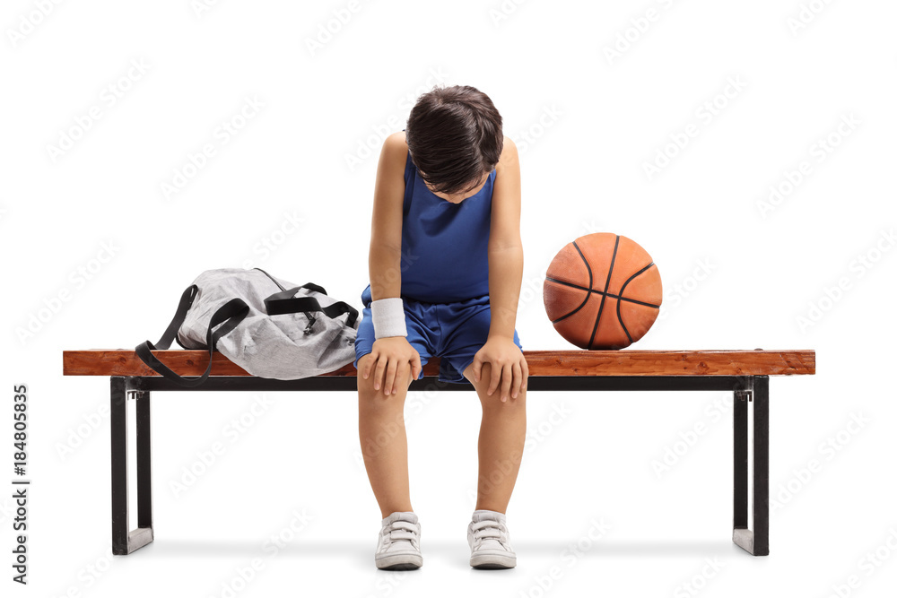 Naklejka premium Sad little basketball player sitting on a bench