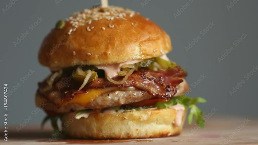 Great Burger with beef cutlet, tomatoes, mushrooms and cucumbers with melted cheese rotates on a wooden Board on light background. Great Burger with beef cutlet, tomatoes, mushrooms and cucumbers with melted cheese rotates on a wooden Board on light background.
