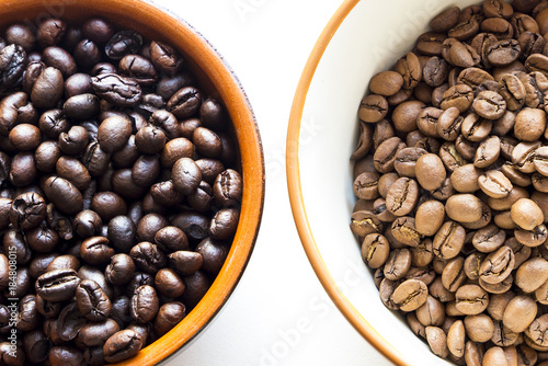 two different types of coffee beans with different roast in cups on a white background
