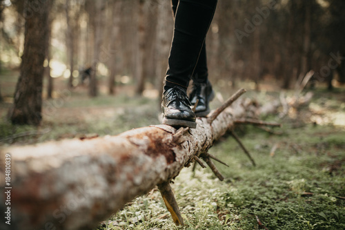 Feet in black shoes walking and balancing on a fallen tree trunk.