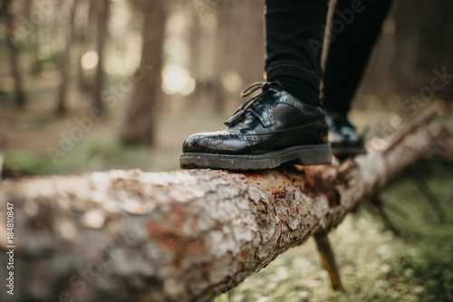 Close up of feet in black shoes walking and balancing on a fallen tree trunk.