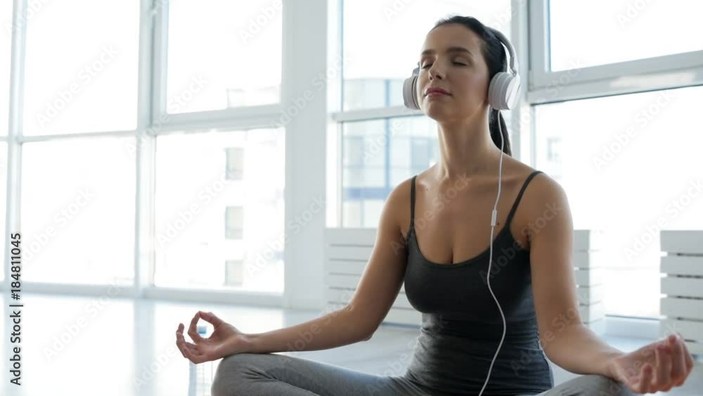 Mind peace. Close up of adorable young woman sitting in yoga position while listening to music and doing meditation Mind peace. Close up of adorable young woman sitting in yoga position while listening to music and doing meditation