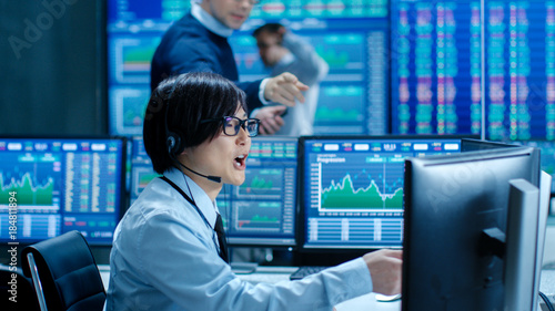 In the Network Operations Senior Trader Dictates Stock Numbers to Their Operator who Makes Call with a Headset. In the Background Traders Discuss Data Shown on Monitors.