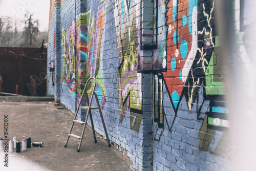 cans with spray paint and ladder near colorful graffiti on wall of building in city © LIGHTFIELD STUDIOS