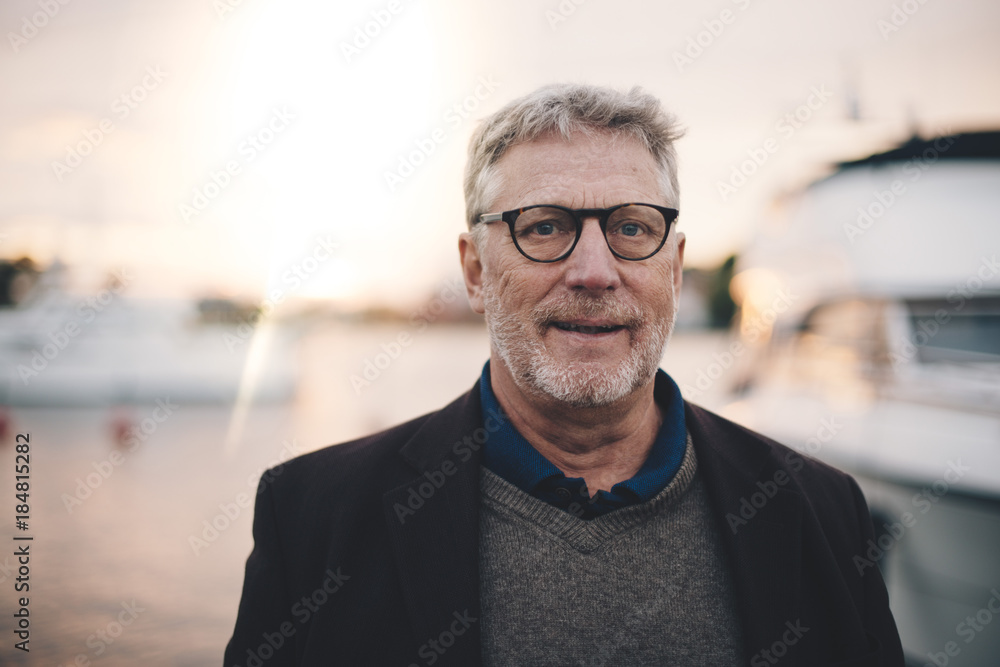 Portrait of senior man smiling at harbor during sunset Portrait of senior man smiling at harbor during sunset