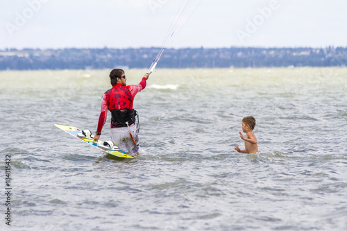 Dad and son are kitesurfing on the sea. The son clings to Papa's back