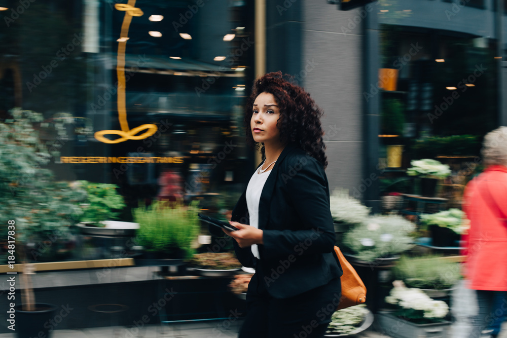 Mid adult businesswoman walking while holding digital tablet against building in city Mid adult businesswoman walking while holding digital tablet against building in city