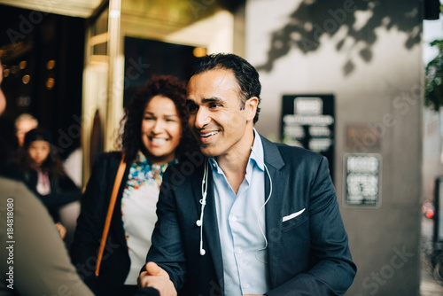 Smiling mature businessman greeting businesswoman while standing by female colleague against building photo
