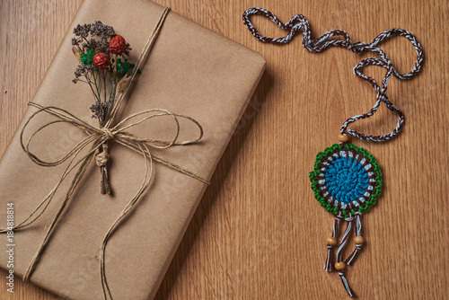 Book is wrapped in brown paper, tied with paper thread lying on the tabletop with an knitted medallion lying next to it.