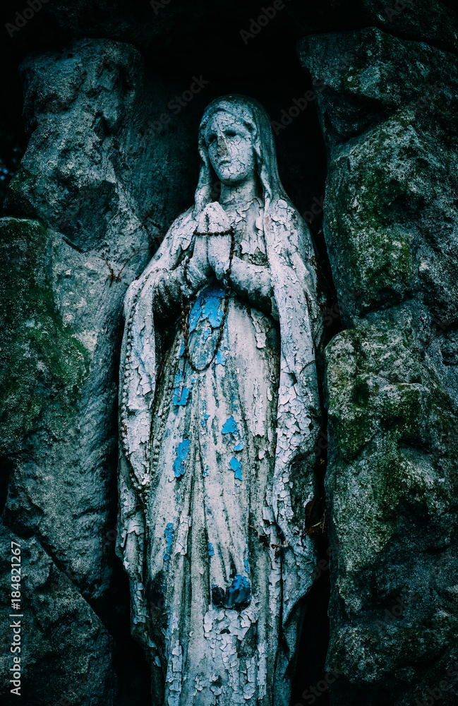 Mystic old statue of the praying madonna. Sad sculpture of the saint lady pray the god.