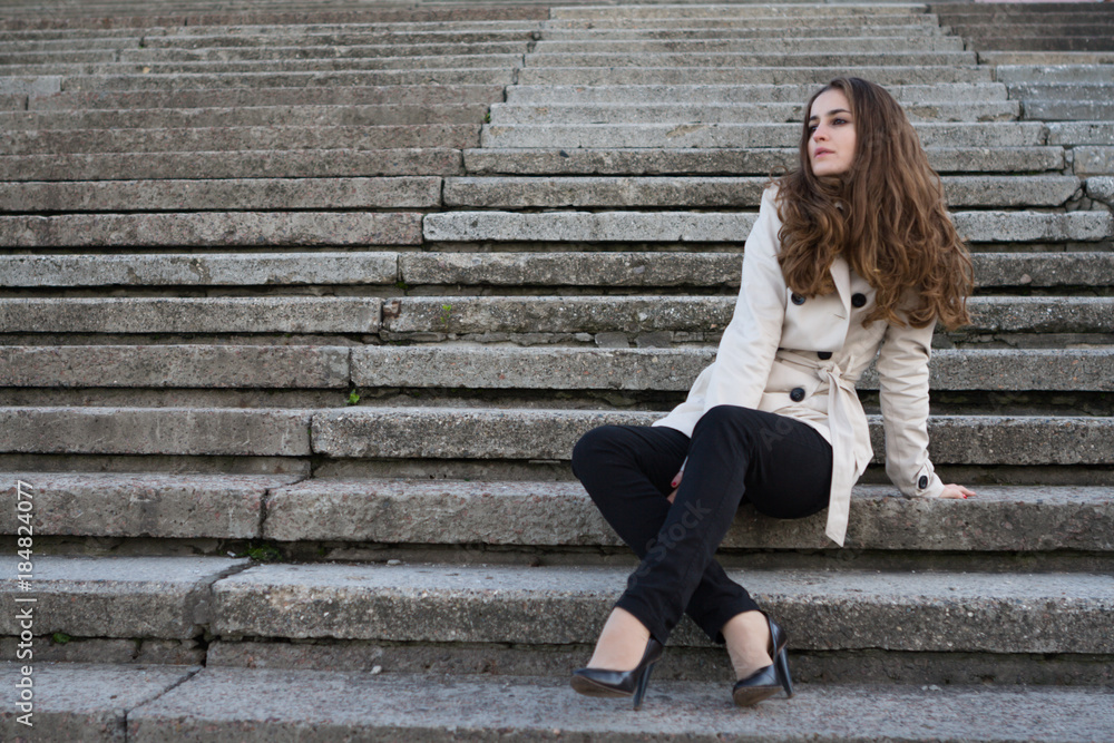 Young beautiful woman wearing beige jacket sitting on concrete stairs Young beautiful woman wearing beige jacket sitting on concrete stairs
