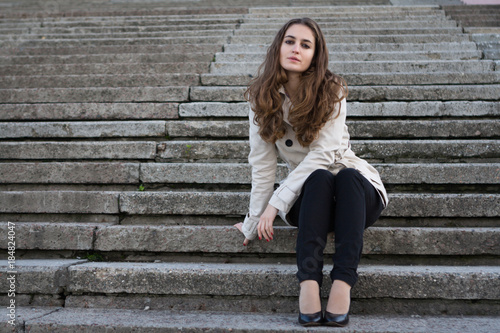 Young beautiful woman wearing beige jacket sitting on concrete stairs